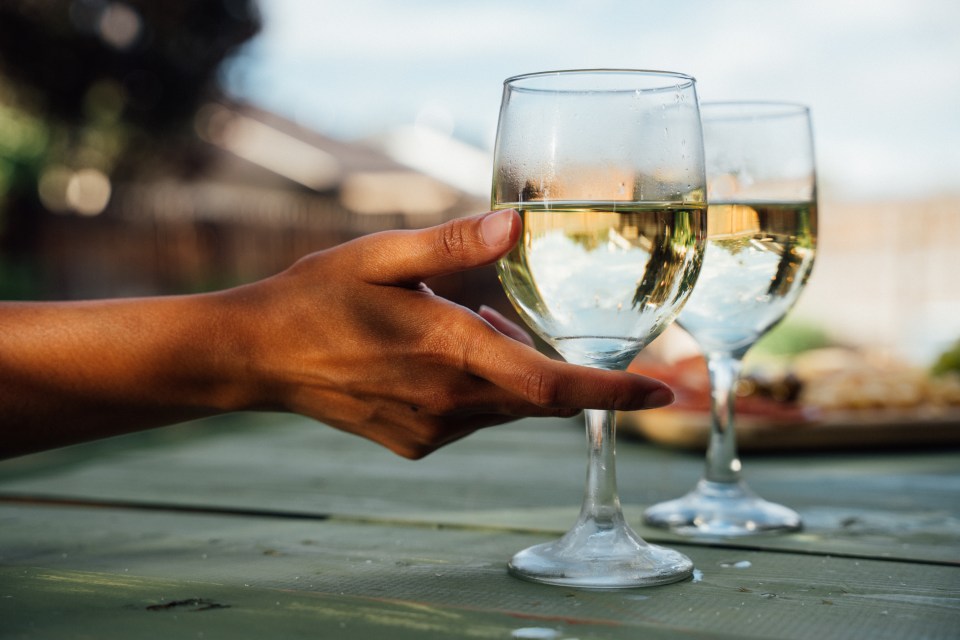 A hand reaching for a glass of white wine at an outdoor gathering.