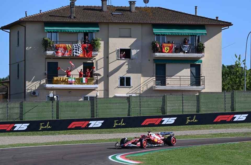 Formula 1 race car driving past spectators on balconies waving flags.