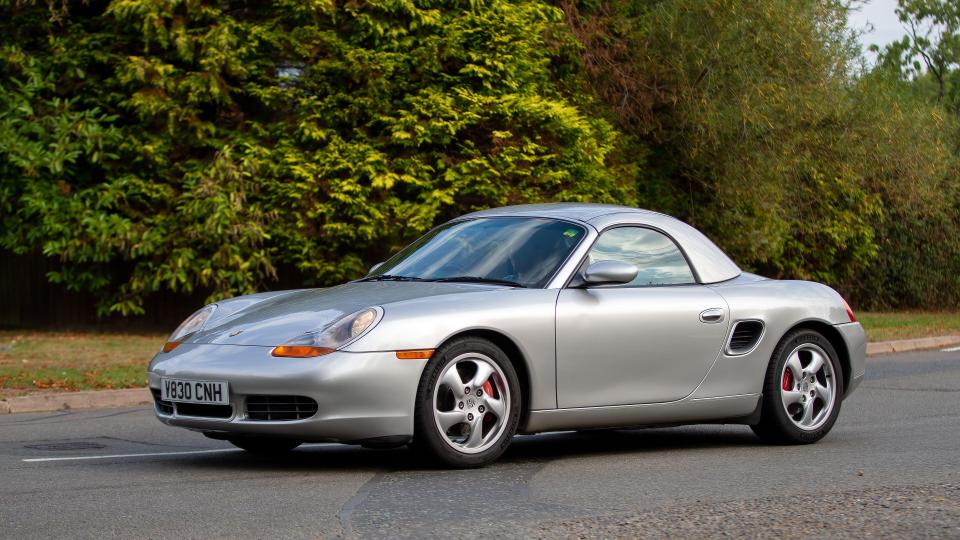 Silver Porsche Boxster driving on a road.