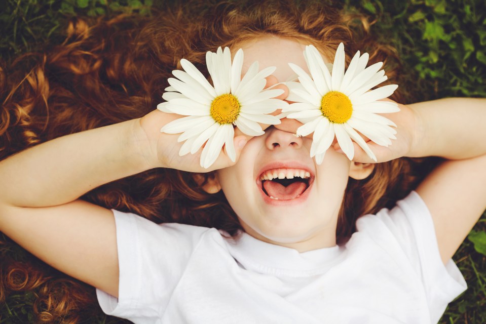 A laughing child with daisies covering their eyes.