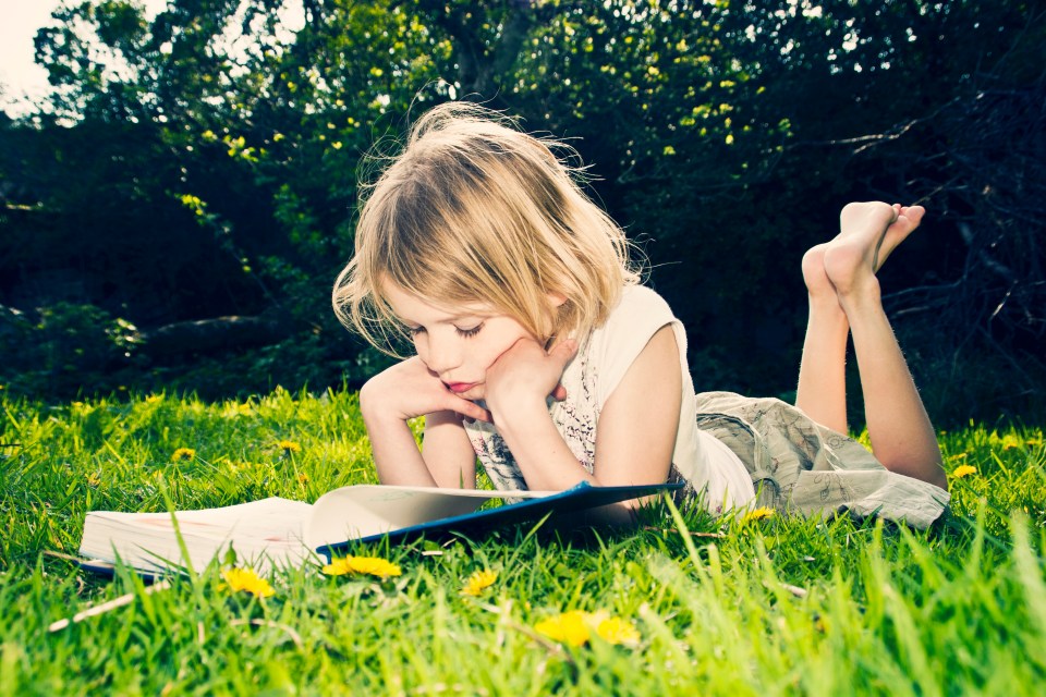 Girl lying on grass reading a book.