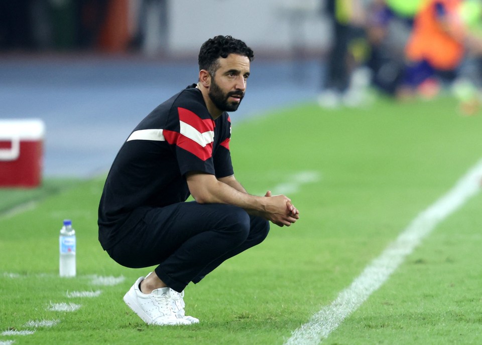 Ruben Amorim, Manchester United manager, crouching on the sidelines of a soccer field.