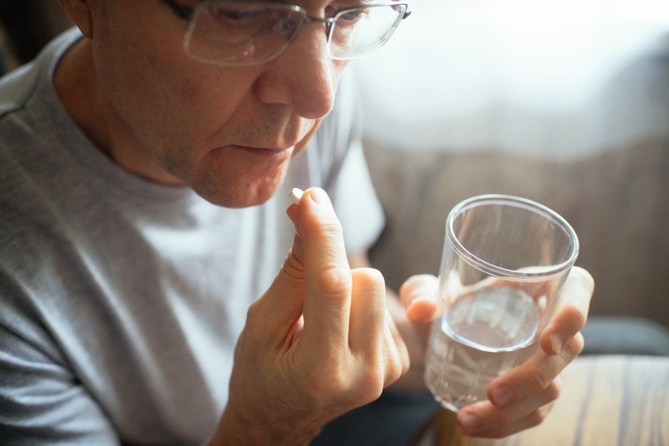 Senior man taking a pill with water.