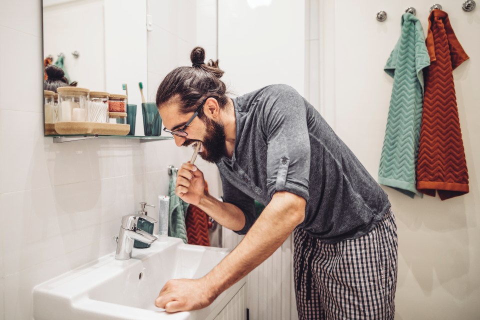 A young man brushing his teeth in a bathroom.