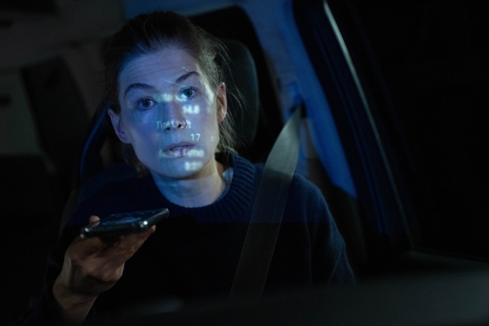 Rosamund Pike in a car at night, using a phone.