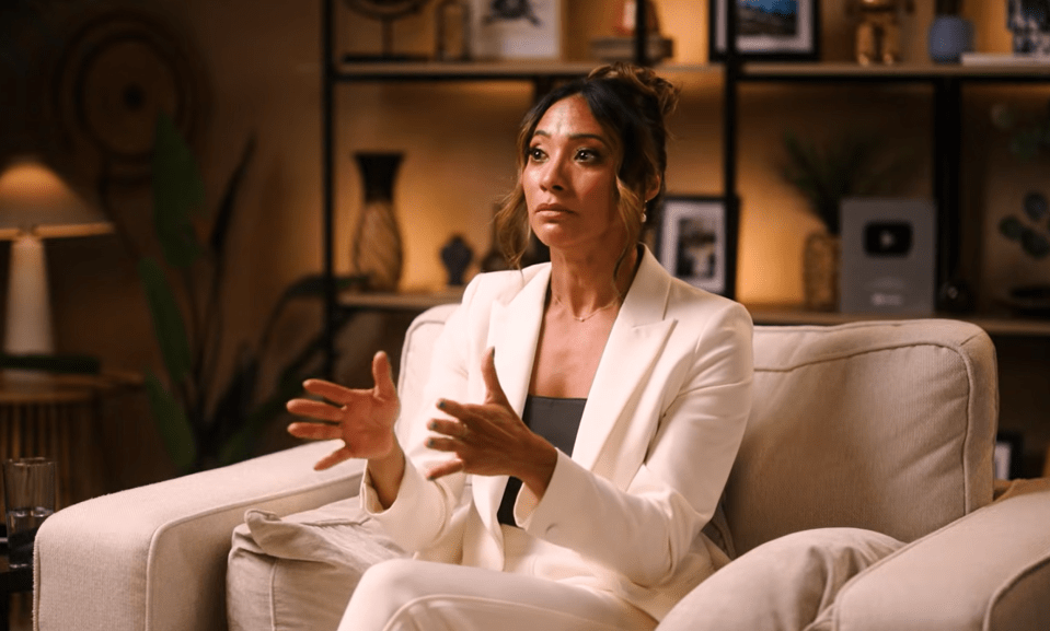 Woman in white suit sitting on a couch, gesturing with her hands.