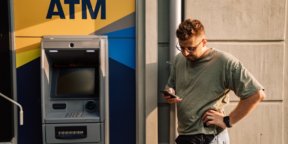 Man using a mobile phone outside an ATM.