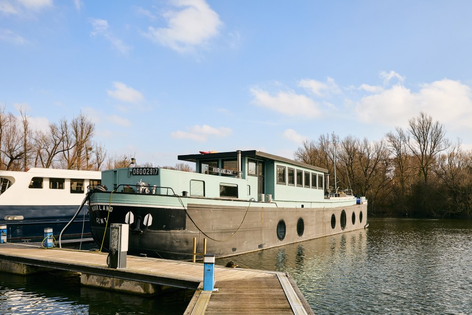 A teal and gray houseboat moored at a marina.