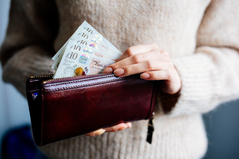 Woman placing British ten-pound notes in a leather wallet.