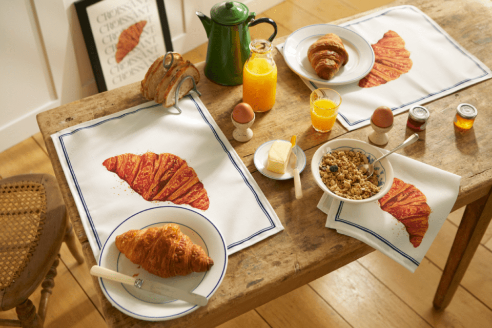 Breakfast table setting with croissants and placemats featuring croissant illustrations.
