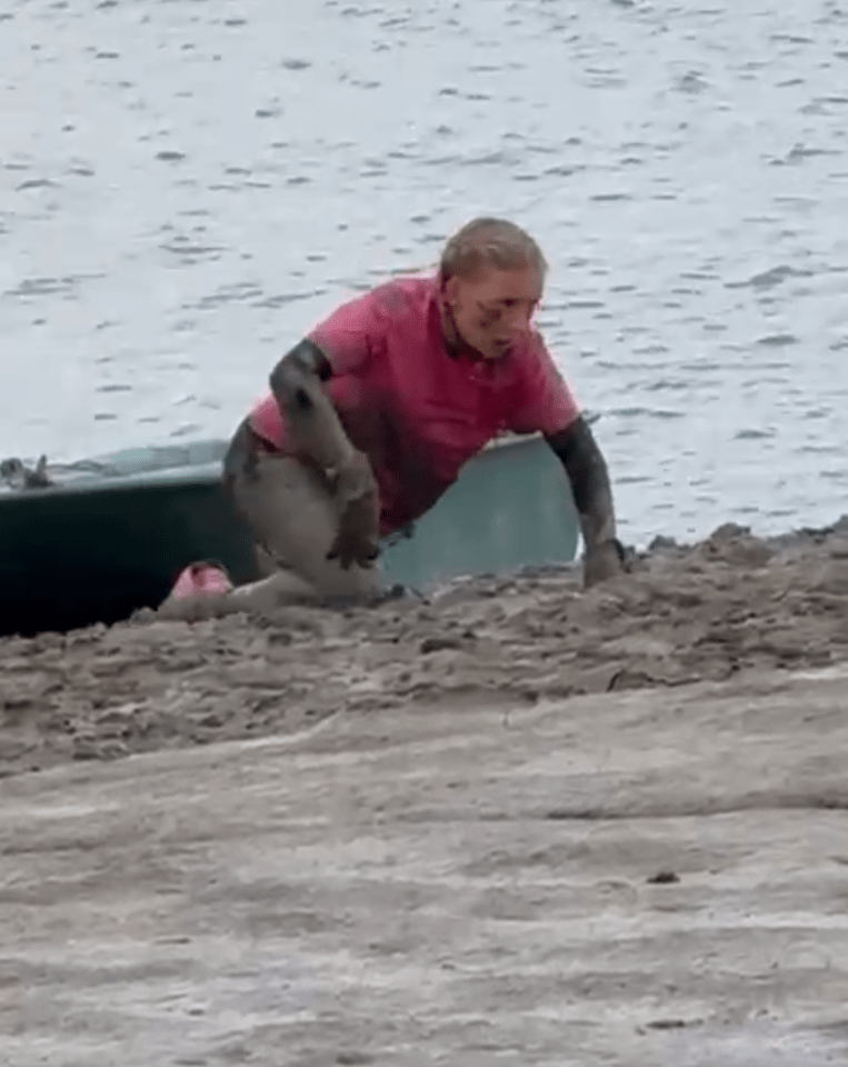 Person covered in mud crawling out of the water.
