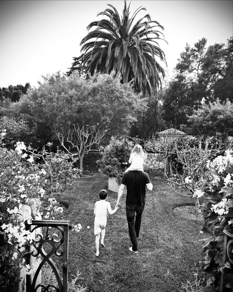Black and white photo of Meghan, Harry, and their children walking in a garden.