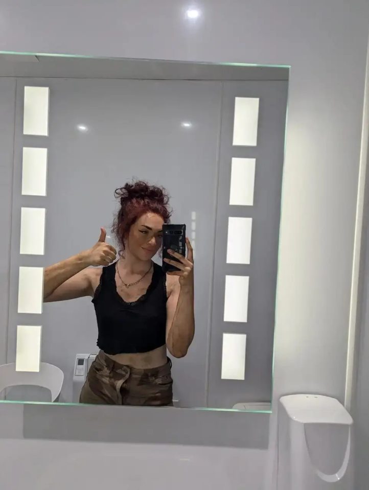 Woman giving thumbs up in bathroom mirror selfie.