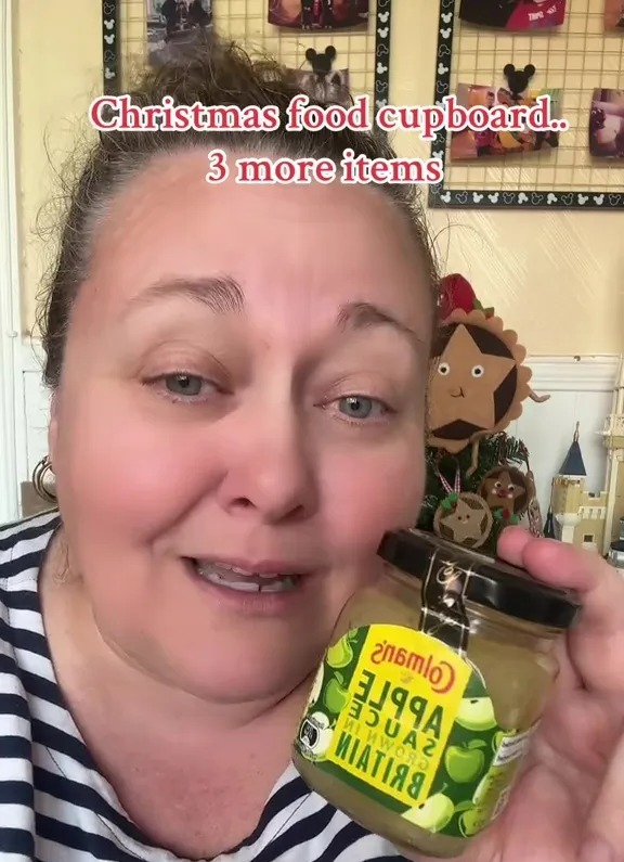 Woman holding a jar of Colman's apple sauce; Christmas food cupboard.