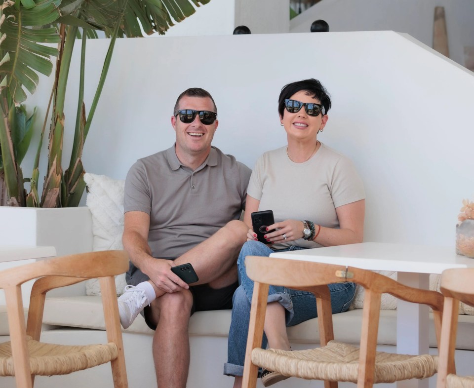 A couple sits on a bench in an outdoor cafe, looking at their phones.