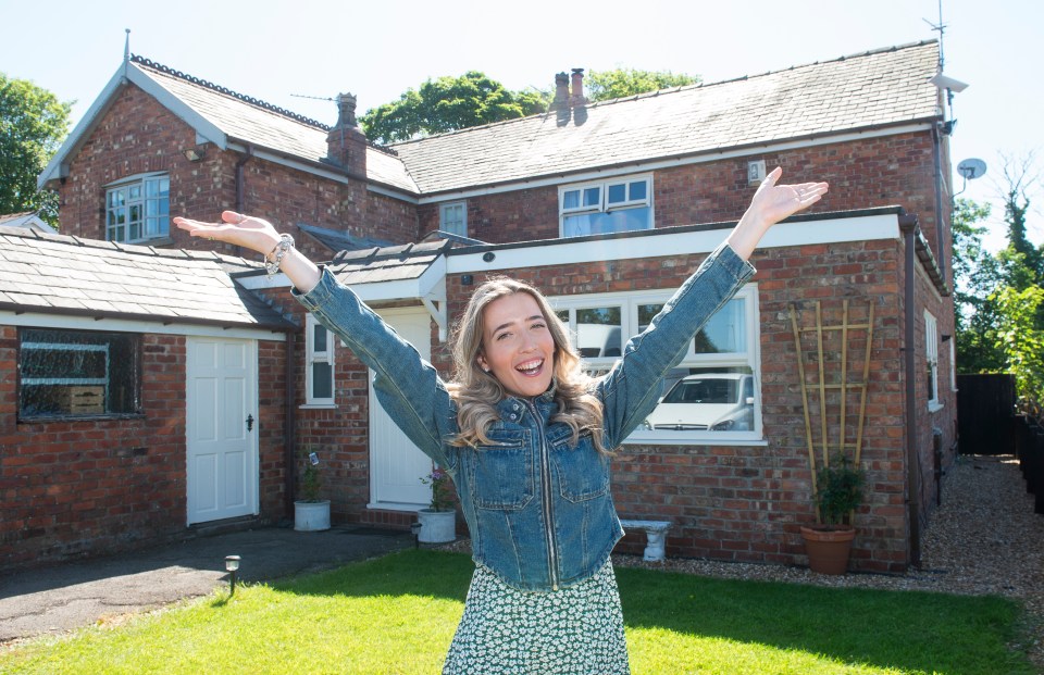 Woman standing in front of her new house with arms outstretched.
