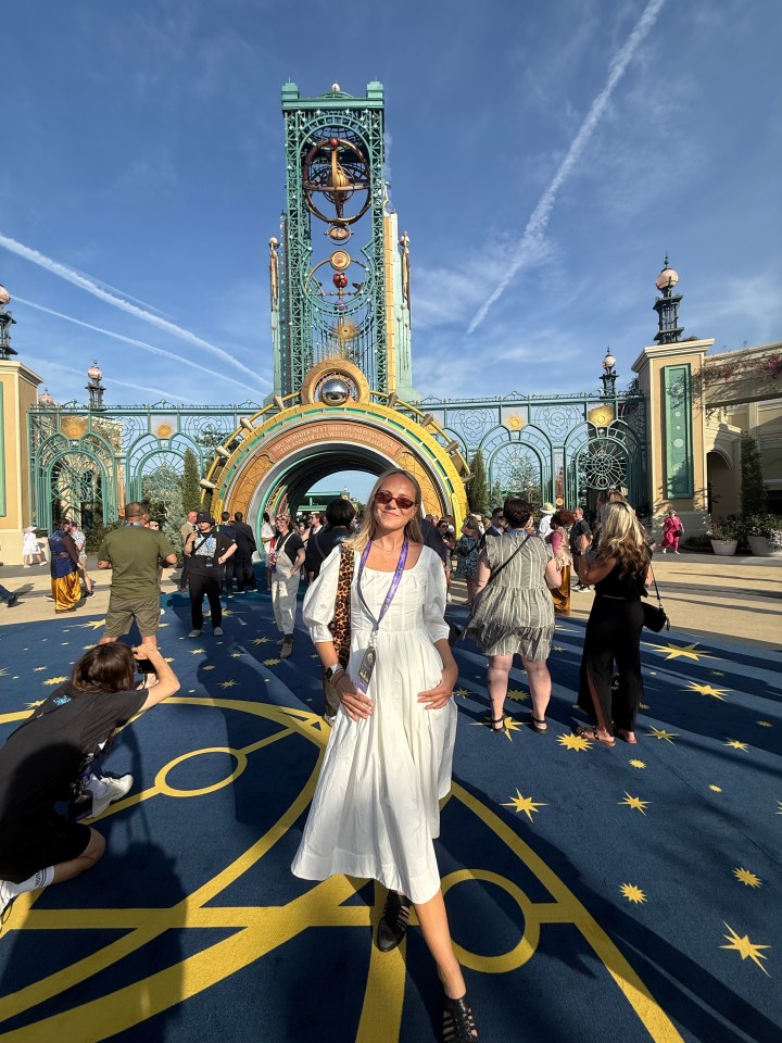 Woman in white dress standing in front of ornate gateway at a theme park.