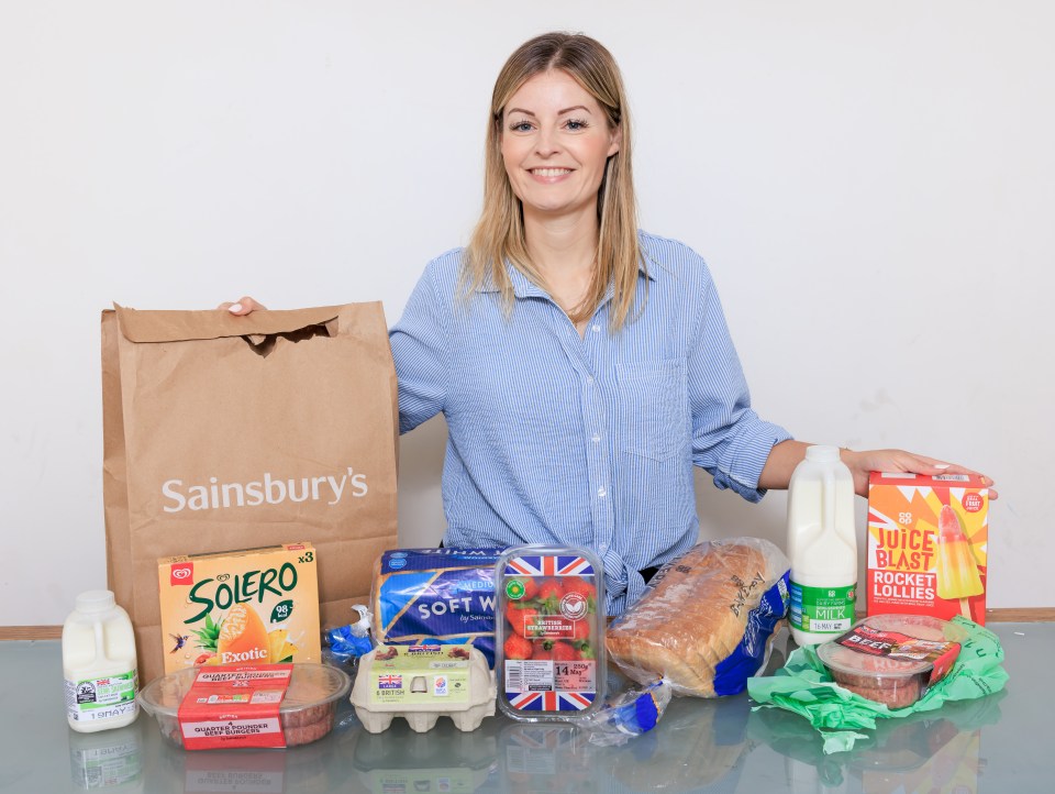 Woman holding Sainsbury's grocery bag with groceries on table.