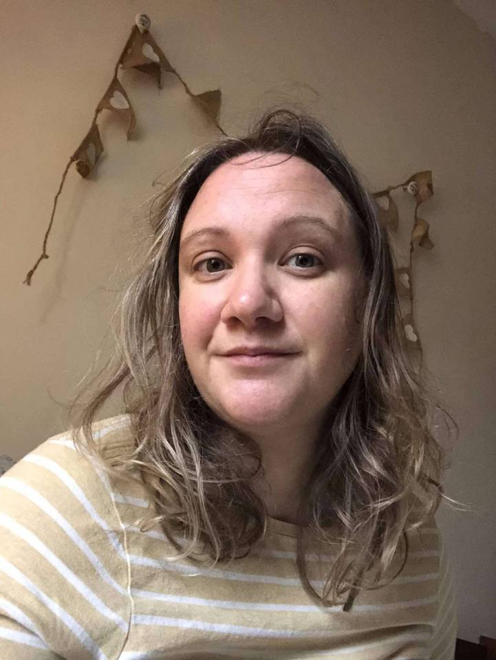 A woman with shoulder-length wavy hair wearing a beige and white striped shirt.