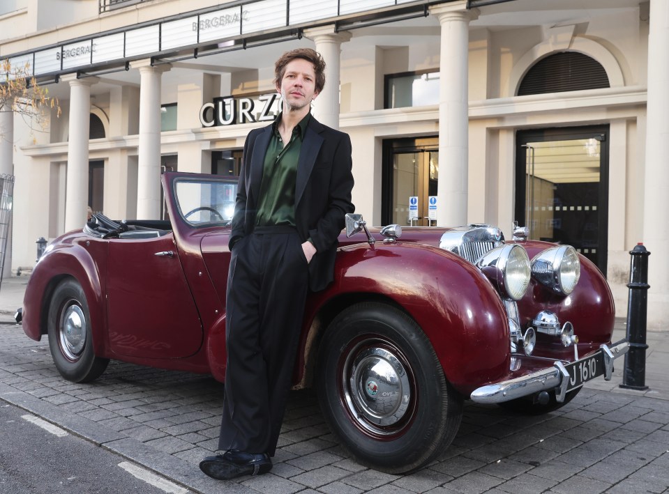 Damien Molony standing next to a vintage car outside a premiere.