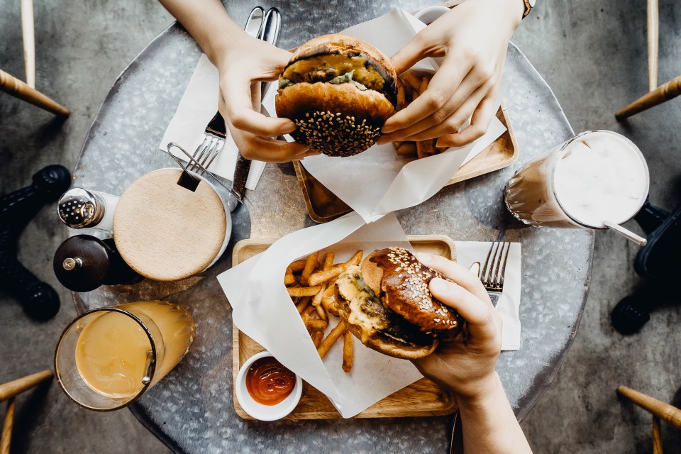 Overhead view of two people sharing burgers and fries at a cafe table.
