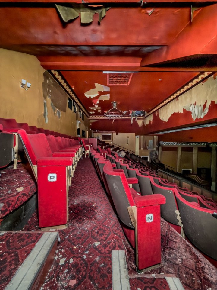 Interior of an abandoned theater with decaying seats and ceiling.