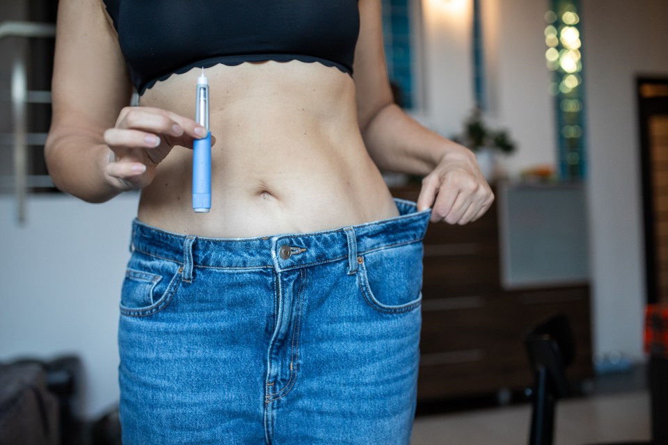 Woman holding semaglutide injector and oversized jeans, celebrating weight loss.