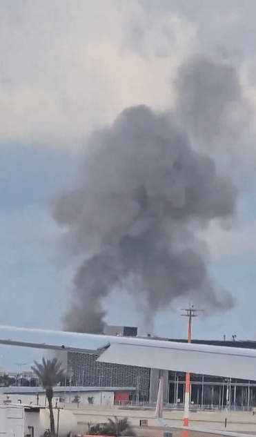 Large plume of smoke rising near an airport building.