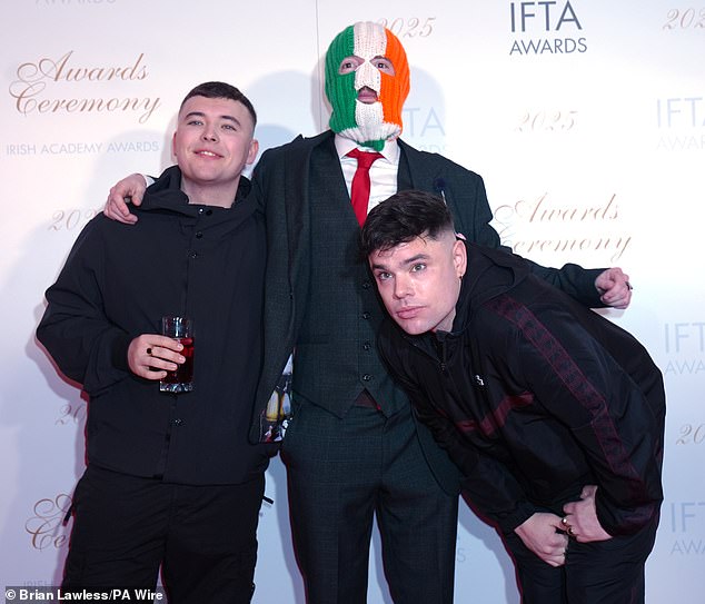 Contoroversial Irish group Kneecap have incited their fans to turn up at court to support them when a band member faces a terror charge. Pictured: Liam O'Hanna, left, with bandmates DJ Provai (centre) and Moglai Bap (right)