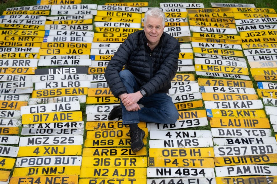 Man sitting amongst hundreds of UK number plates.