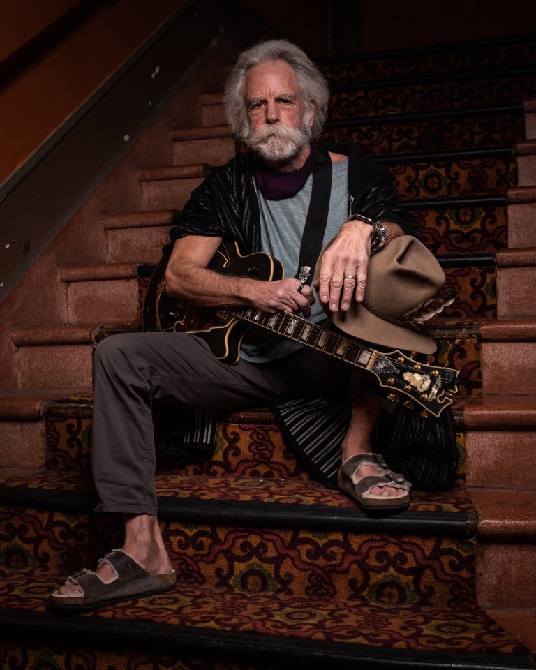 Bobby Weir sitting on stairs with guitar.