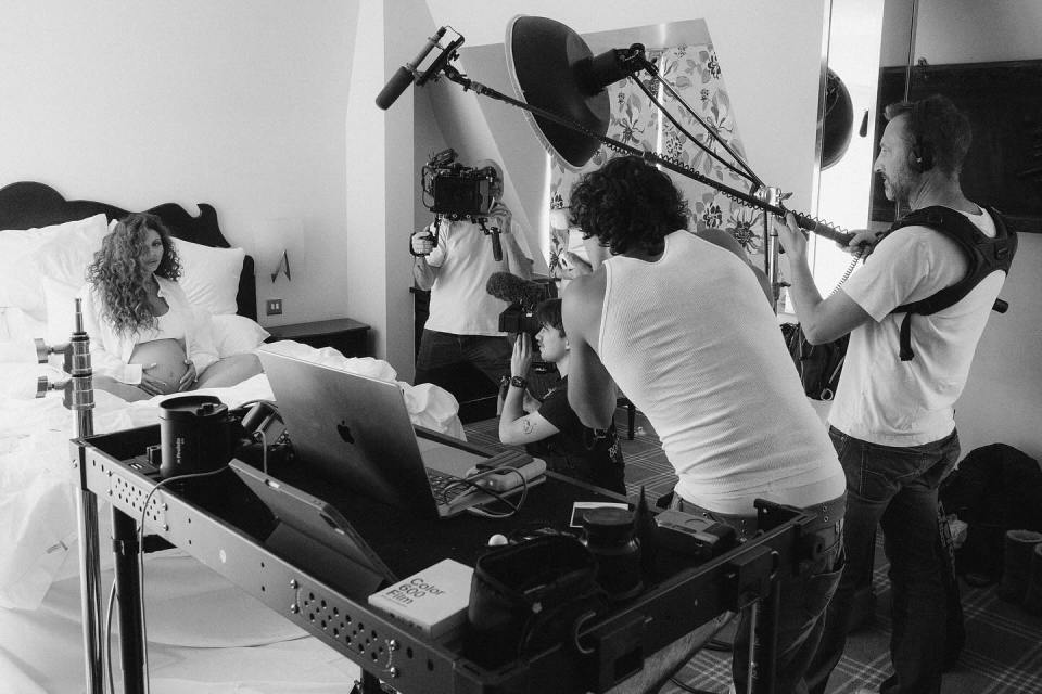 Black and white photo of a film crew filming a pregnant woman in a hotel room.