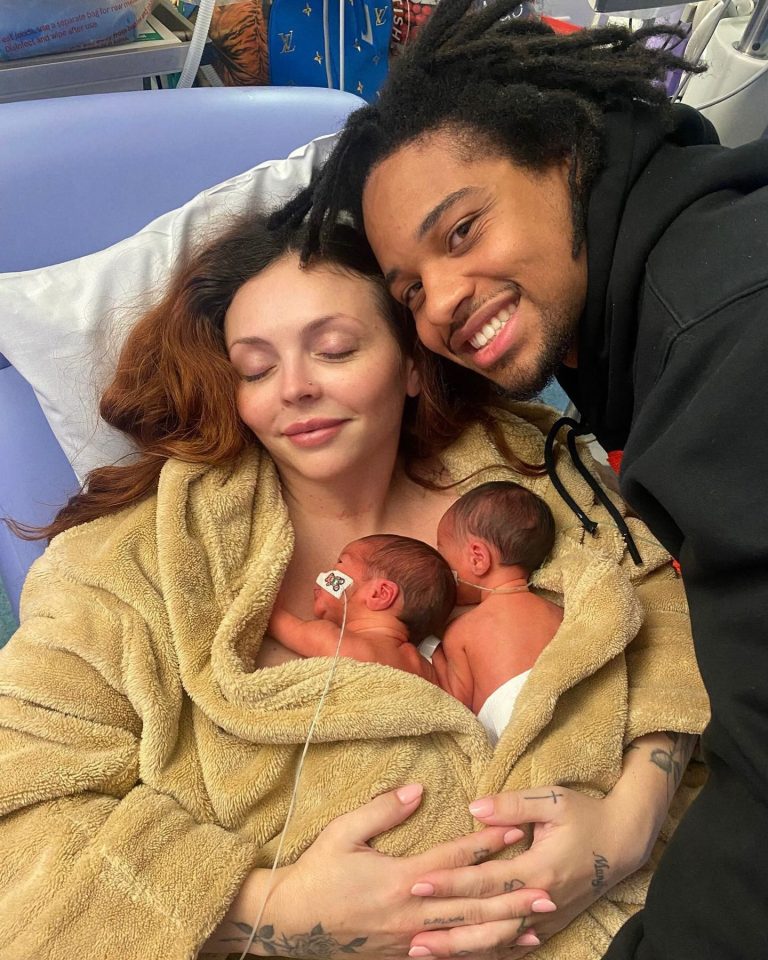 A mother and father cuddling their newborn twin daughters in a hospital bed.