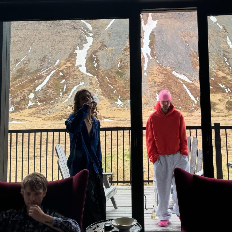 Justin Bieber and another person on a balcony overlooking a mountain landscape.  One person appears to be smoking.