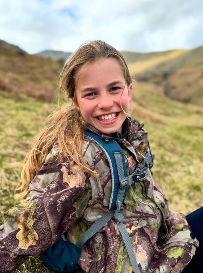 Smiling girl wearing camouflage jacket and backpack.