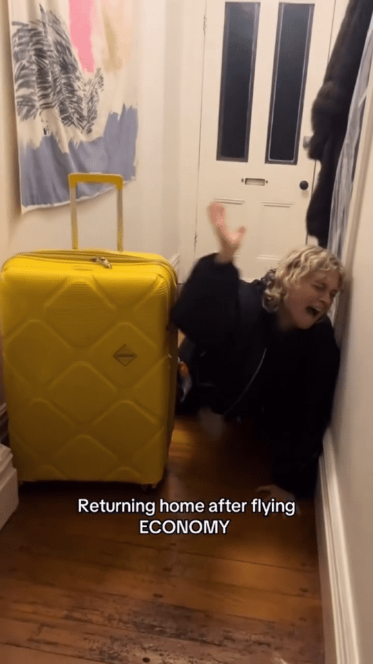 Woman dramatically leaning against a wall after arriving home from an economy flight.