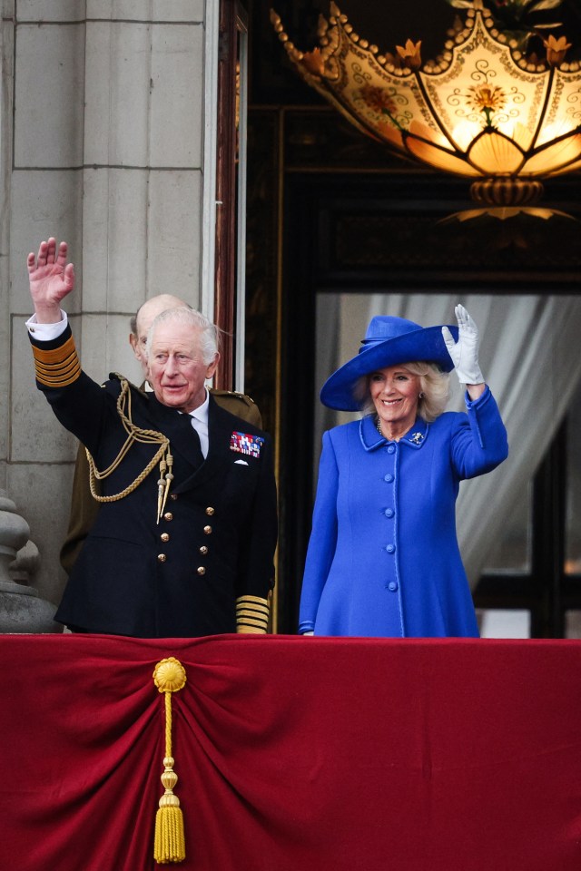 King Charles III and Queen Camilla waving from Buckingham Palace balcony.