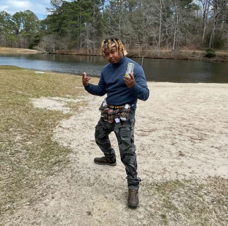 Man holding a can, wearing camouflage pants and a bandolier.
