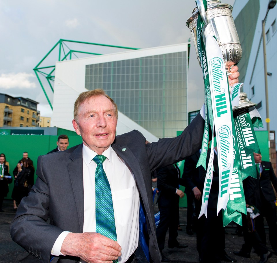 Portrait of an older man in a suit, standing in front of a stadium.