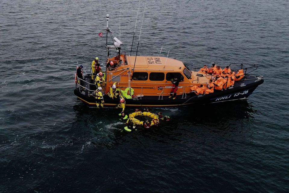 An image collage containing 1 images, Image 1 shows RNLI lifeboat crew rescuing migrants in the English Channel