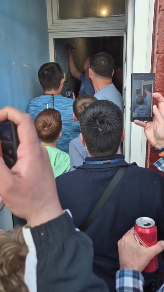 A crowd of people gathered outside a doorway, one person is writing on the door.