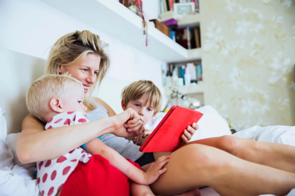 Woman and two children looking at a tablet in bed.