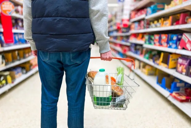 Person in a supermarket pushing a shopping basket with groceries.