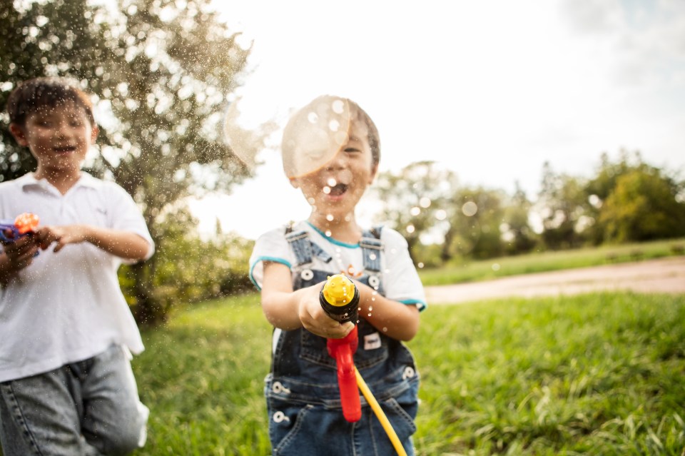 Two young boys playing with water guns outside.