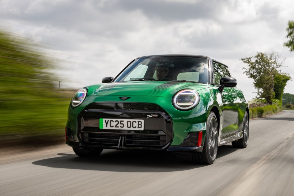 Green Mini Cooper driving down a road.
