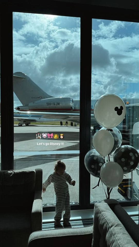 Toddler by window looking at private jet with Mickey Mouse balloons.