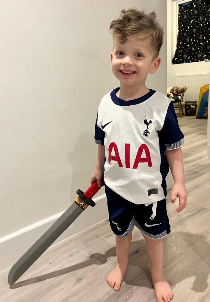 Three-year-old boy holding a toy sword, wearing a Tottenham Hotspur football kit.