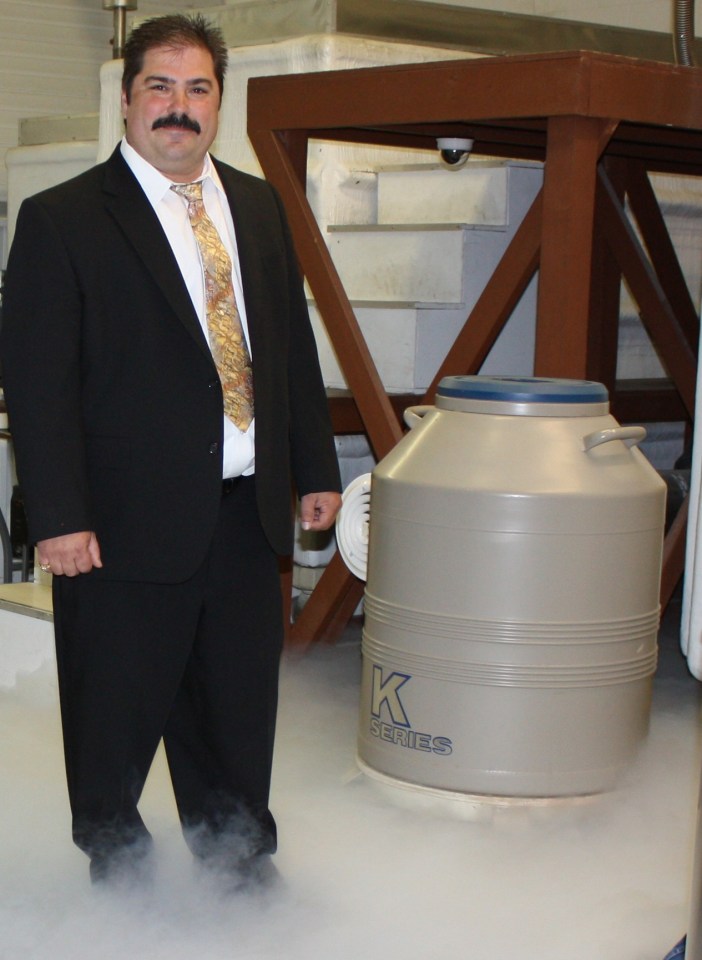 Man in suit standing next to cryogenic tank.