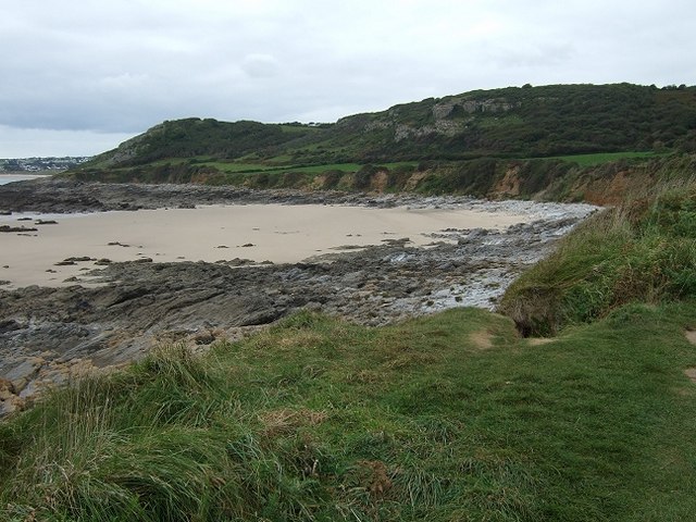 Sandy beach with rocky shoreline and grassy cliffs.