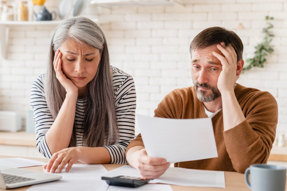 Worried middle-aged couple reviewing financial documents.
